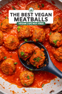 Vegan Meatballs in saute pan with marinara sauce topped with fresh parsley. A wooden spoon holds 2 meatballs in the pan