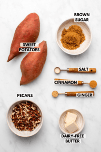 Ingredients for Stovetop Candied Sweet Potatoes in small bowls on marble background. Clockwise text labels read brown sigar, salt, cinnamon, ginger, dairy-free butter, pecans, and sweet potatoes