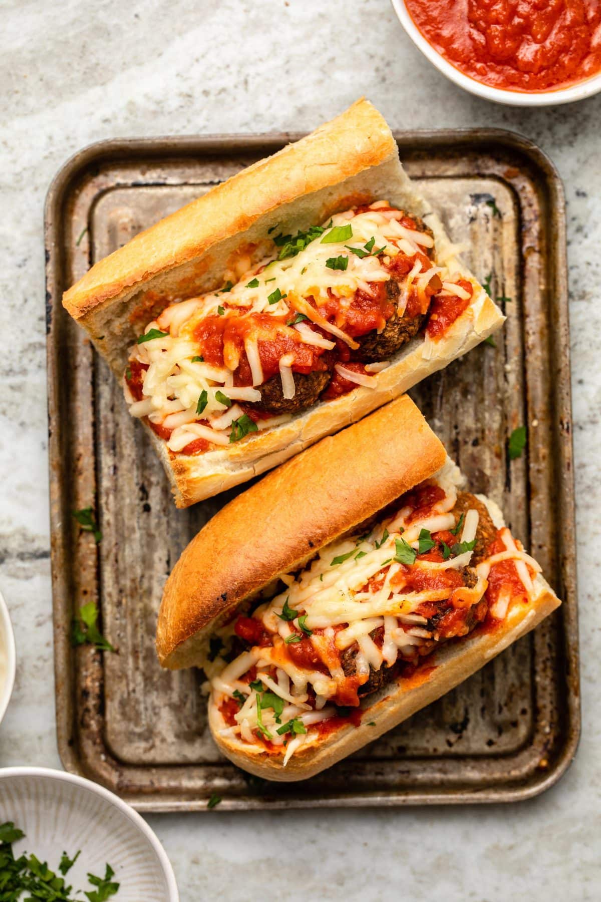 Meatball sub with french bread, meatballs, sauce, cheese, and parsley on small baking tray