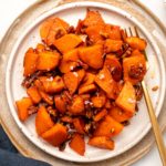 Stovetop Candied Sweet Potatoes with Pecans on white plate with gold fork on marble background
