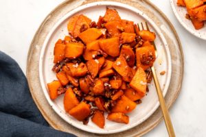 Stovetop Candied Sweet Potatoes with Pecans on white plate with gold fork on marble background