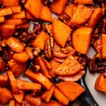 Stovetop candied sweet potatoes in grey pan with navy spatula scooping some of them up