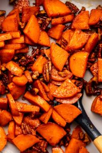 Stovetop candied sweet potatoes in grey pan with navy spatula scooping some of them up