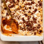 Vegan Sweet potato casserole topped with toasted marshmallows and pecans, in a white baking dish on marble countertop