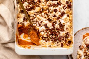 Vegan Sweet potato casserole topped with toasted marshmallows and pecans, in a white baking dish on marble countertop