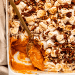 Close-up photo of baked sweet potato casserole with gold spoon in baking dish scooping some of the casserole out
