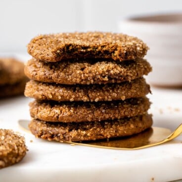 Stack of chewy ginger molasses cookies on white serving tray with more cookies in the background