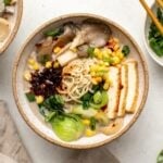 Bowl of ramen with mushrooms, pak choy, corn, tofu, chili oil, and green onions