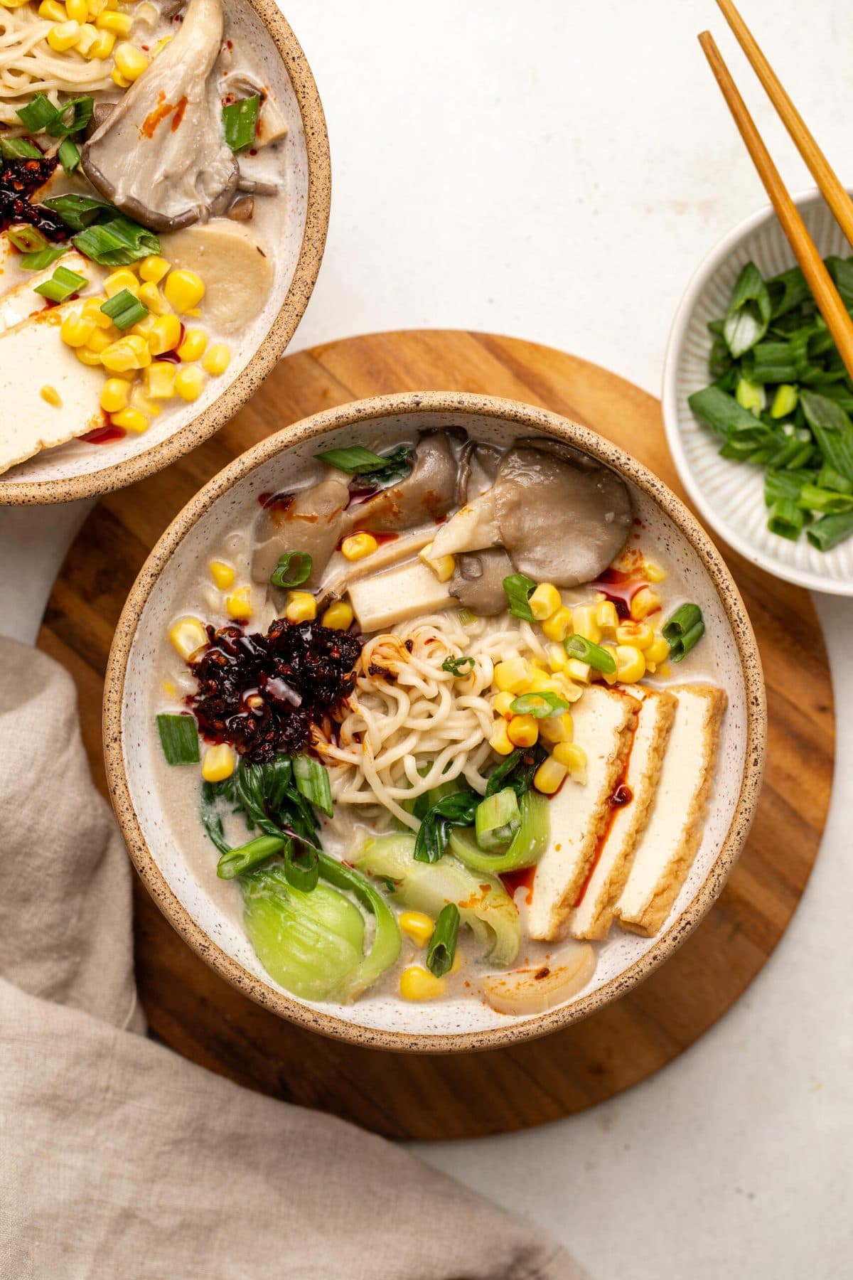 Two bowls of vegan mushroom ramen topped with tofu and corn on stone countertop
