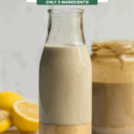 glass bottle of tahini dressing next to sliced lemons with jar of tahini in the background