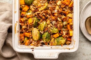 Roasted vegetables and pecans in white casserole dish on stone countertop
