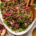 Lentil salad with pomegranate, parsley, and pickled red onions in white serving bowl with wooden serving spoons