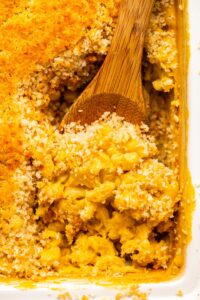 Close-up photo of wooden spoon scooping baked mac and cheese out of white casserole dish