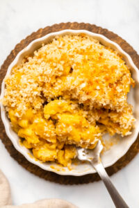 Close-up photo of baked mac and cheese in small scalloped bowl with a fork scooping a bite of the pasta