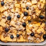 French toast casserole in baking dish topped with blueberries, powdered sugar, and maple syrup