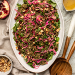 Lentil salad with pomegranate, parsley, and pickled red onions in white serving bowl with wooden serving spoons