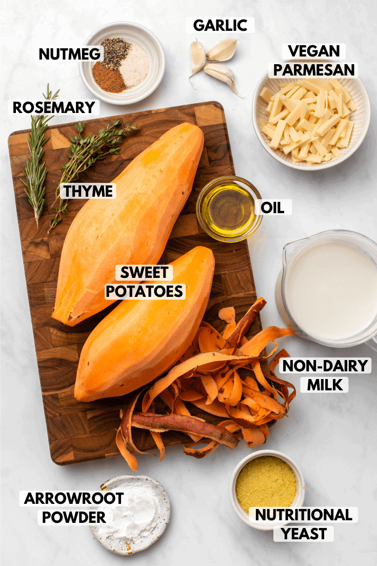 Ingredients for sweet potato gratin on marble background. Clockwise text labels read garlic, vegan parmesan, oil, non-dairy milk, nutritional yeast, arrowroot powder, sweet potatoes, thyme, rosemary, and nutmeg
