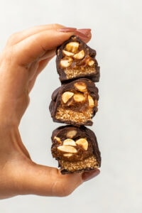 hand holding stack of 3 snickers bars stacked on top of each other and sliced open to show texture