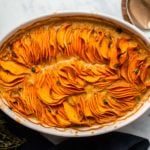 Sweet potato gratin topped with fresh thyme in baking dish with navy linen and gold serving spoon