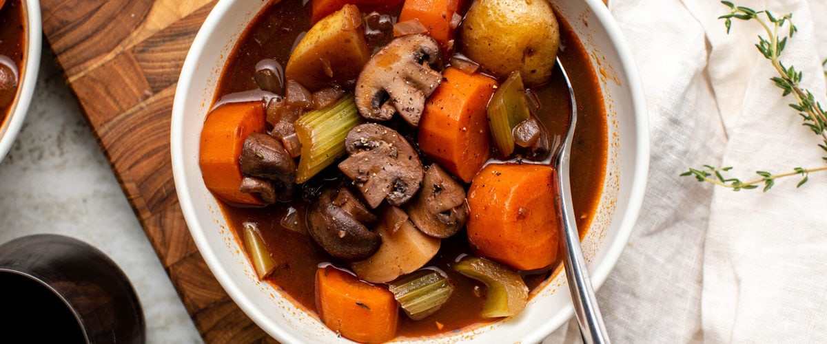 Bowl of vegan stew on wood cutting board with white linen on the side