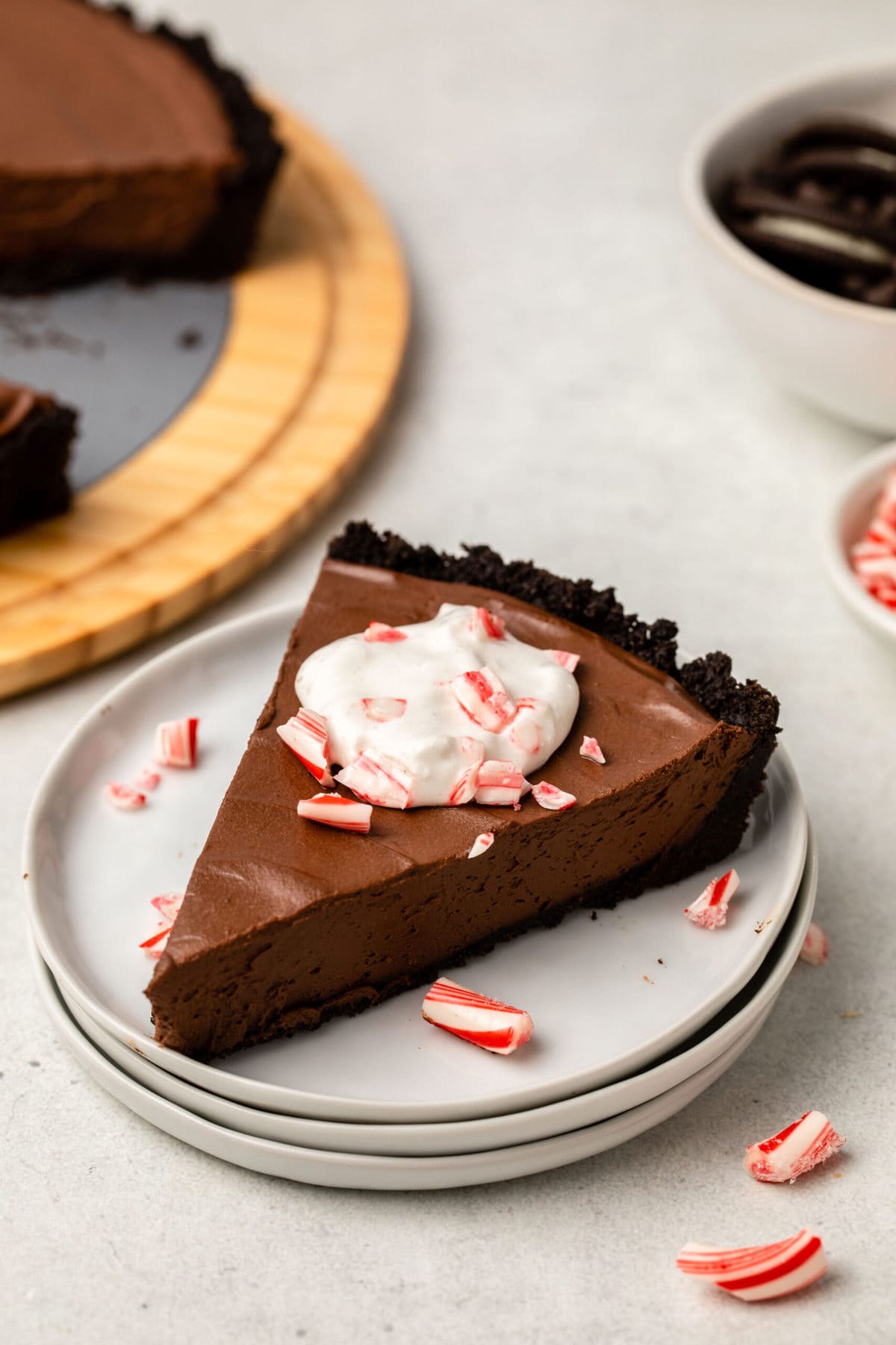 Slice of chocolate peppermint pie topped with whip cream and candy cane pieces on stack of white plates