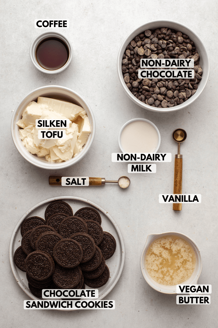 Ingredients for no-bake chocolate peppermint pie in small bowls on countertop. Clockwise text labels read chocolate chips, oat milk, peppermint extract, vegan butter, oreos, salt, silken tofu, and maple syrup