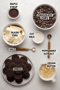 Ingredients for no-bake chocolate peppermint pie in small bowls on countertop. Clockwise text labels read chocolate chips, oat milk, peppermint extract, vegan butter, oreos, salt, silken tofu, and maple syrup