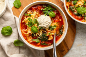 Two bowls of vegan lasagna soup topped with fresh herbs, vegan ricotta, and vegan mozzarella