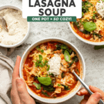 Hands holding a bowl of vegan lasagna soup topped with vegan ricotta cheese and fresh basil