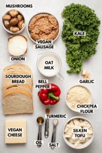 Ingredients for vegan strata in small bowls on kitchen countertop. Clockwise text labels read kale, garlic, oat milk, chickpea flour, silken tofu, salt, turmeric, oil, vegan cheese, sourdough cheese, bell pepper, onion, mushrooms, and vegan sausage