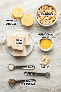 Ingredients for vegan ricotta arranged on kitchen countertop. Clockwise text labels read cashews, nutritional yeast, garlic, pepper, italian seasoning, salt, firm tofu, and lemon juice and zest