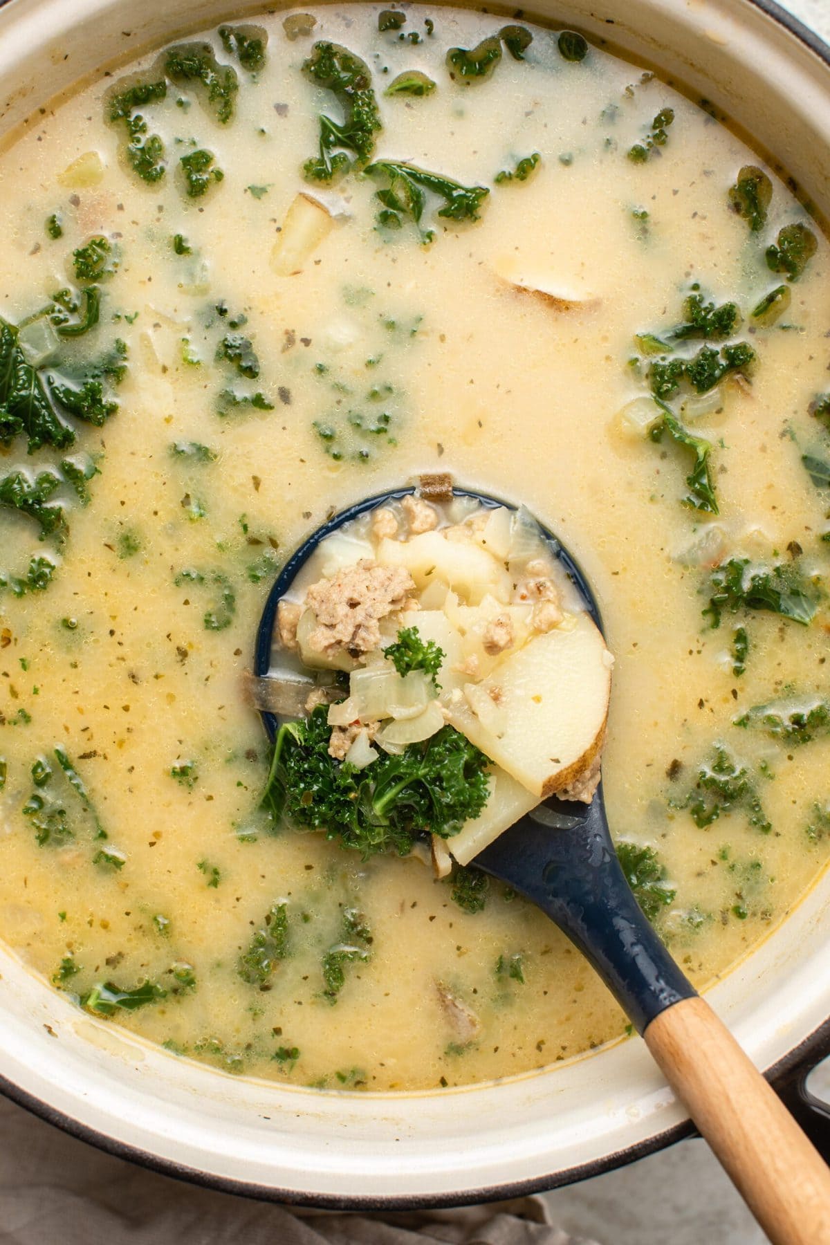 Cooked soup in large pot with spoon scooping out creamy broth, sausage, potatoes, and kale