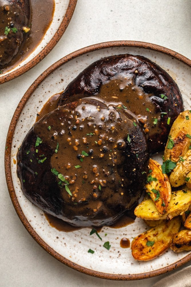 Two mushroom steaks topped with peppercorn sauce on white plate