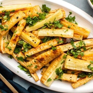 Roasted parsnips topped with gremolata on white plate on countertop