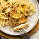 Close-up photo of piccata with slice cut into it and pasta with lemon sauce on the side