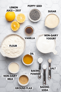 Ingredients for muffins on tiled countertop in small bowls. Clockwise text labels read poppy seed, sugar, non-dairy yogurt, salt, baking soda, baking powder, ground flax, non-dairy yogurt, flour, vanilla, and lemon juice and zest