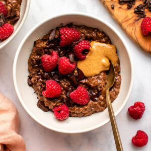 Bowl of chocolate oatmeal topped with chocolate raspberries and nut butter