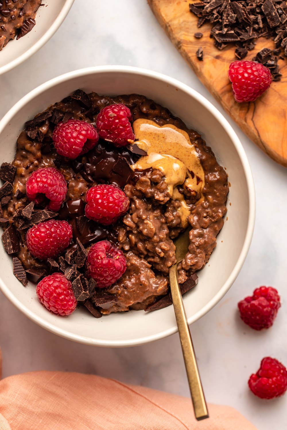 Chocolate oatmeal in bowl with more chocolate, raspberries, and nut butter