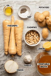 Ingredients for parsnip soup on countertop. Clockwise text labels read potatoes, cashews, lemon, vegetable broth, garlic, onion, parsnips, oil, and salt and pepper