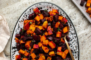 Roasted sweet potatoes and beets with spices on white serving tray with gold spoon