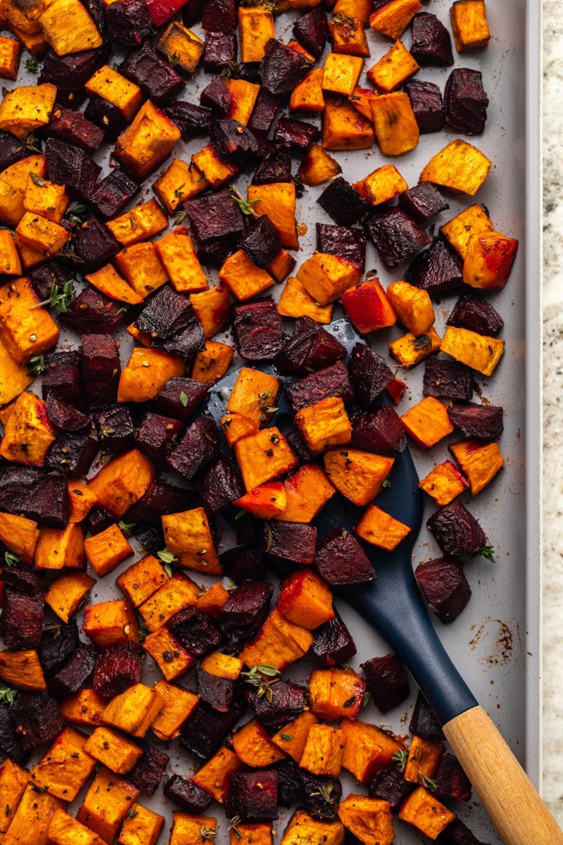roasted sweet potatoes and beets on baking sheet with wooden serving spatula