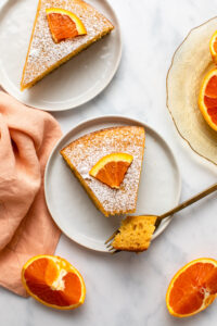Slices of orange cake on small white plates on marble countertop