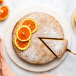 Vegan Orange Cake topped with powdered sugar and orange slices with slice cut out of it