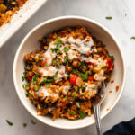 Stuffed Pepper casserole in white bowl topped with melty vegan cheese and parsley