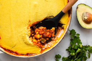 Spoon scooping serving out of tamale pie baked in round cast iron pan