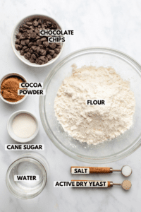 Ingredients for no-knead chocolate bread in small bowls on marble countertop