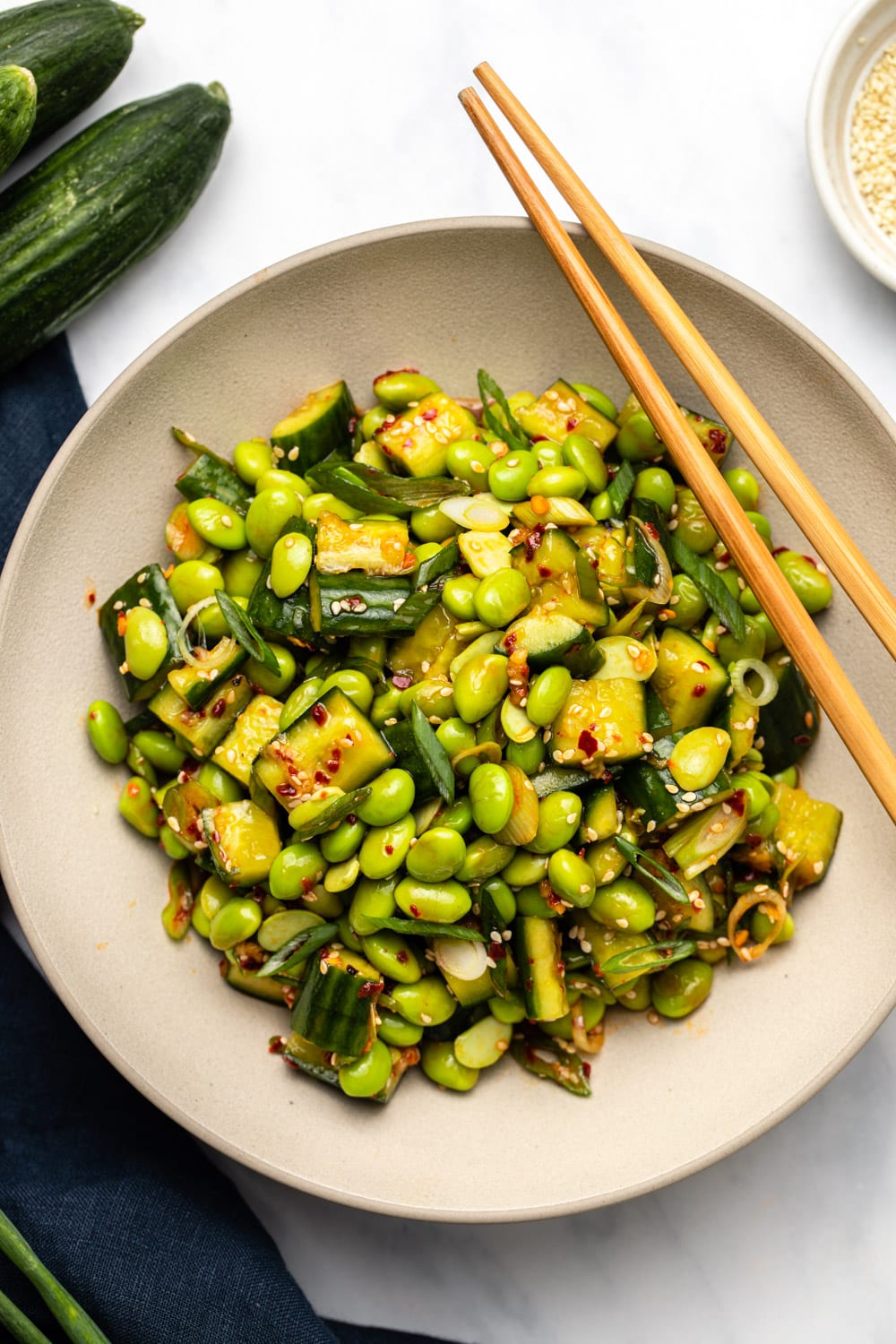 Edamame salad in bowl with chopsticks and persian cucumbers on the side