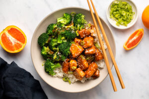 Orange tofu with broccoli and rice in bowl with chopsticks