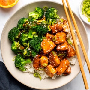 Orange tofu with broccoli and rice in bowl with chopsticks