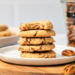 stack of pecan sandies on white plate with jar of pecans in the back